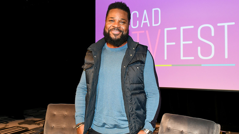 Malcolm-Jamal Warner smiling while posing for photos in a gilet and blue jumper