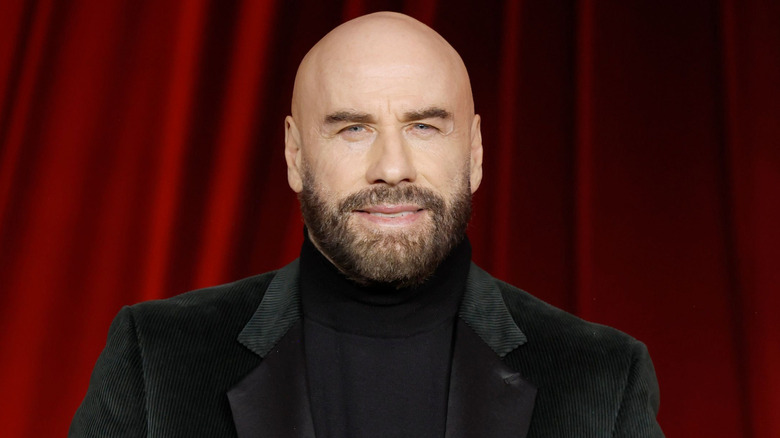 John Travolta stands in front of a red curtain