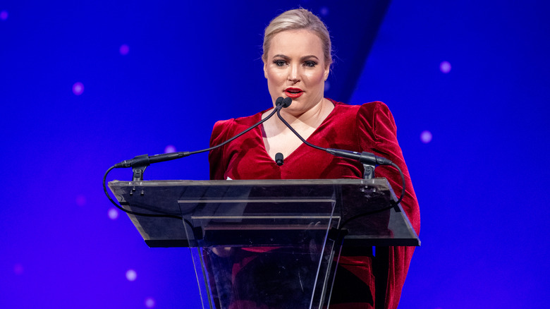 Meghan McCain speaking onstage at an event in a red dress
