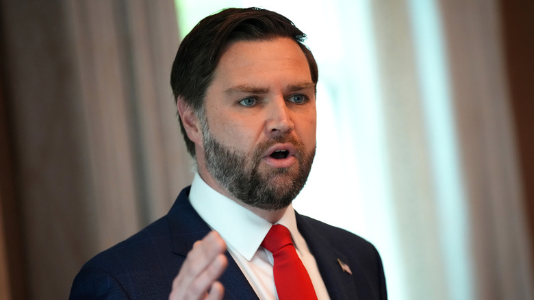 JD Vance speaking at an event while holding his hand up