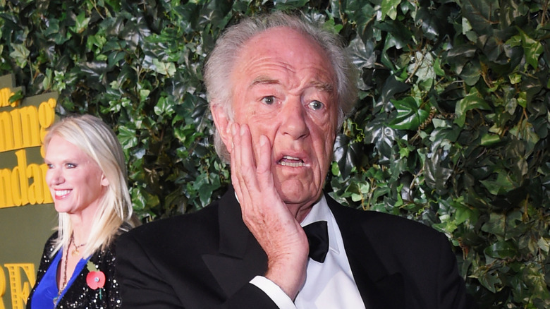 Michael Gambon touching face and looking alarmed