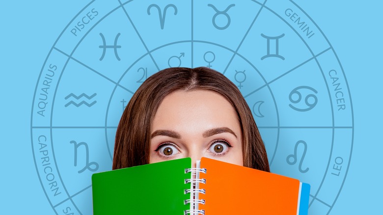 A woman holding a book near a zodiac circle. 