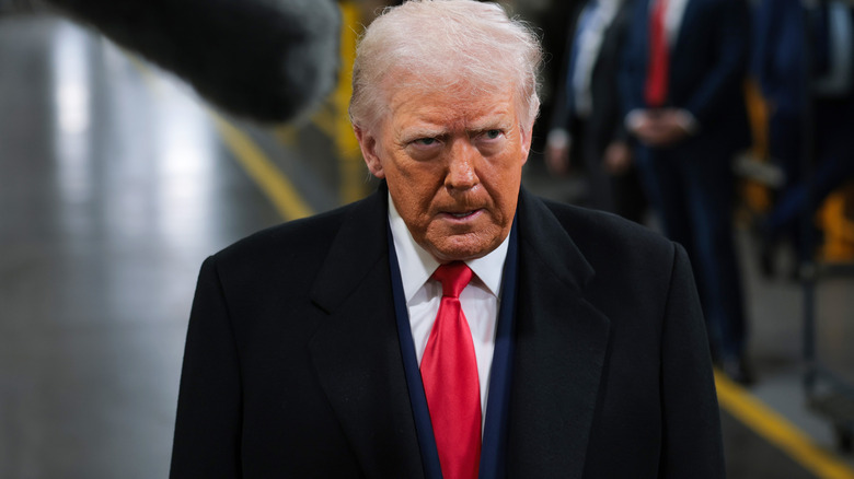 Donald Trump looking furious in a black suit with a white shirt and a red tie