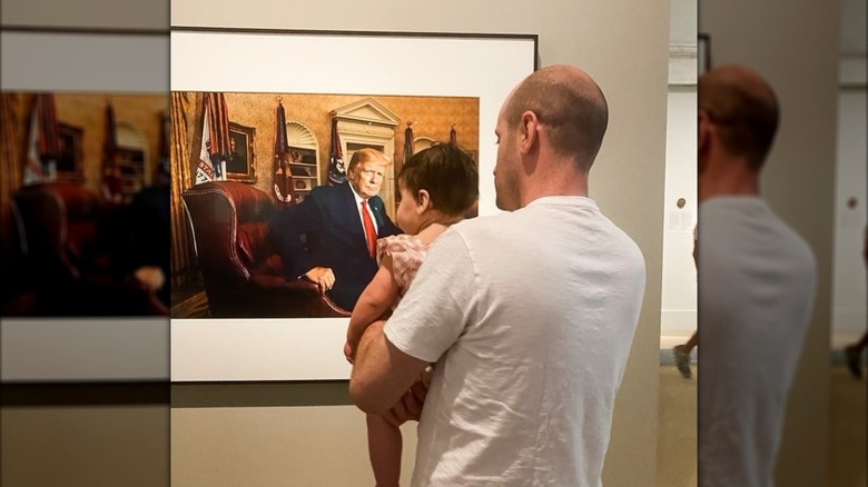 Stephen Miller holds his daughter while admiring a photo of Donald Trump