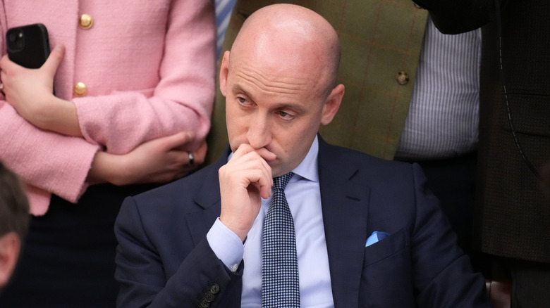 Stephen Miller looking uncomfortable with his hand to his mouth in a dark suit