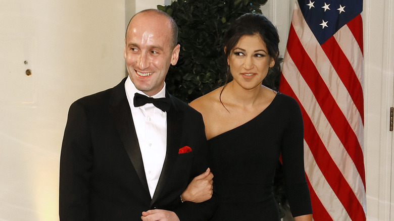 Stephen Miller smiling in a tuxedo while arm in arm with his wife in a black dress