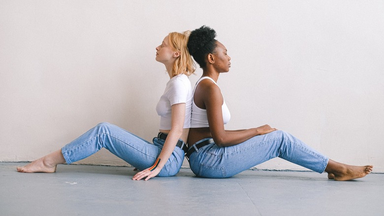 women sitting back to back in jeans