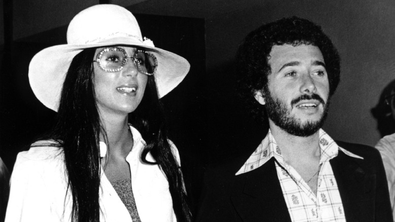 Cher smiling in glasses and hat with David Geffen