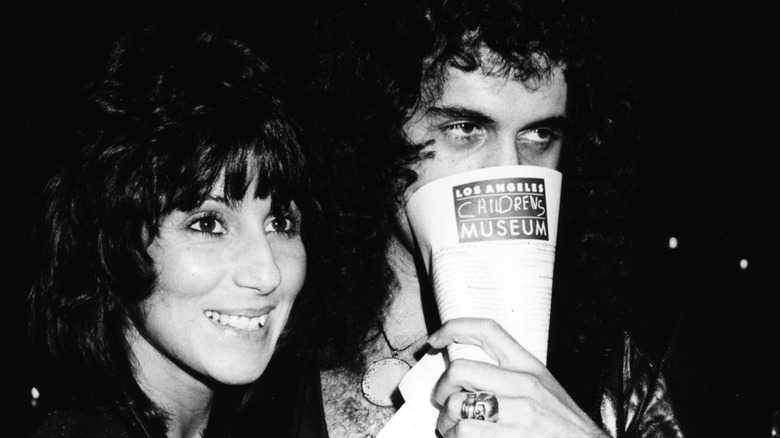 Gene Simmons covering his face beside a smiling Cher