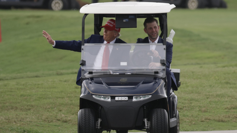 Eric Trump driving his father in a golf cart while the latter waves at bystanders