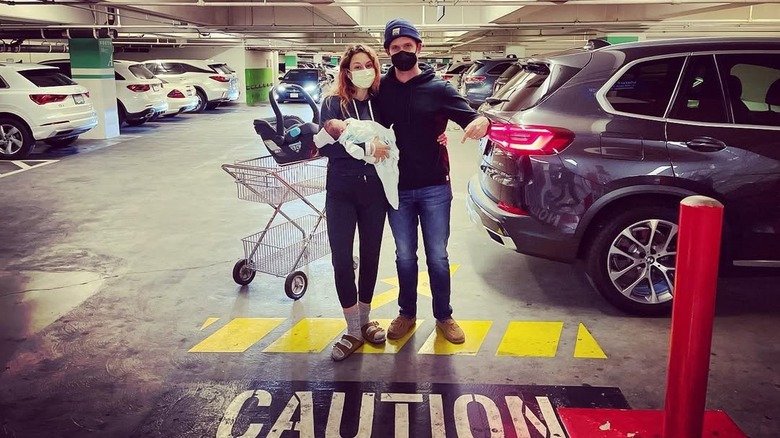 Troian Bellisario and Patrick J. Adams posing with their daughter Elliot in a hospital parking lot