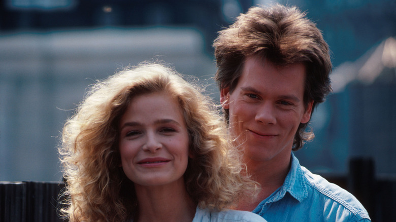 Kyra Sedgwick smiling while standing in front of Kevin Bacon