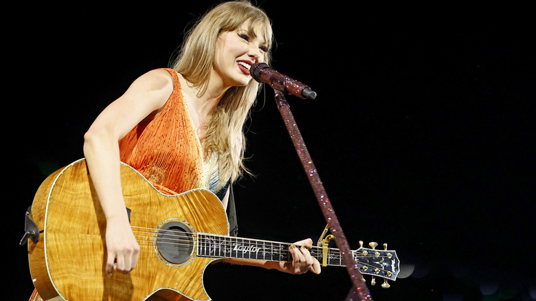 Taylor Swift dressed in orange performing onstage during the Eras tour