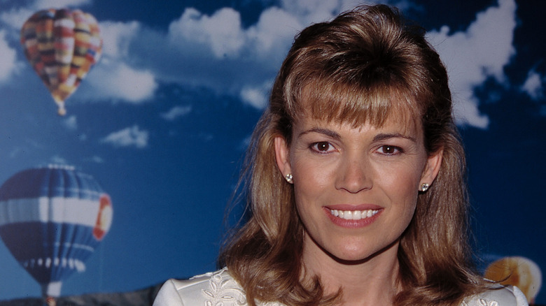 Vanna White standing in front of a background with clouds and hot air balloons