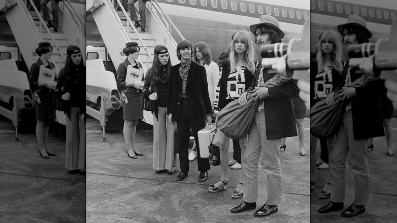 Pattie Boyd and George Harrison standing with Ringo Starr, Maureen Cox, and Eric Clapton by an airplane