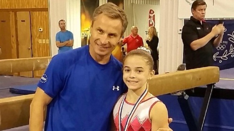 Olivia Dunne as a child posing with medal around her neck next to her coach