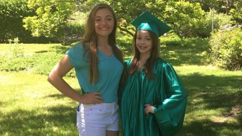 Olivia Dunne as a kid in cap and graduation gown in her garden with her sister