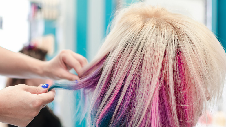 Woman with multi-colored hair and a cowlick gets it style by another woman.