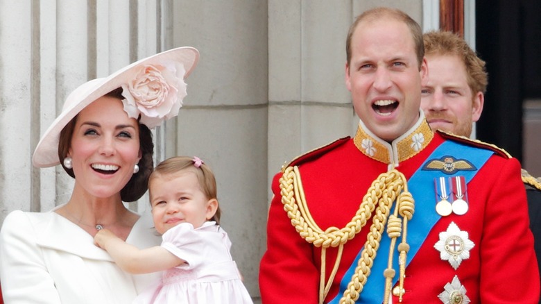 Kate Middleton holding a young Princess Charlotte at 2016 Trooping the Colour, with Prince William standing in front of Prince Harry to the right