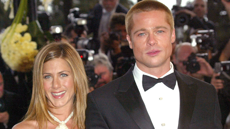 Jennifer Aniston smiling in a white dress next to Brad Pitt who's wearing a suit and bowtie at the premiere of 'Troy.'