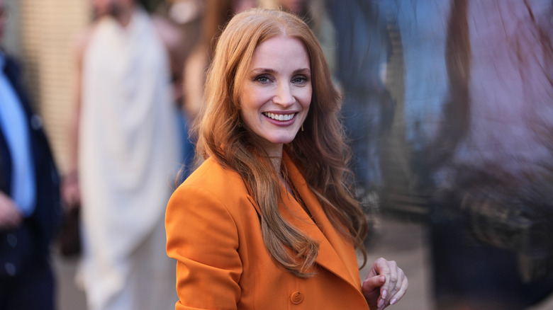 Jessica Chastain smiling and wearing orange at Paris Fashion Week in 2026.