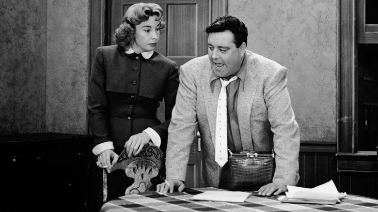 Audrey Meadows and Jackie Gleason standing near a table in "The Honeymooners."