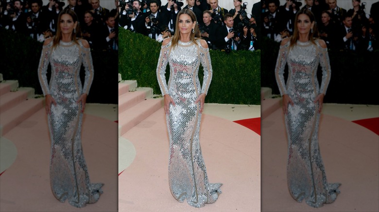 Cindy Crawford at the MET Gala in a silver floor length dress with shoulder cut-outs and nude colored panelling
