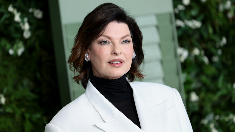 Linda Evangelista posing while wearing a white jacket over a black turtleneck.