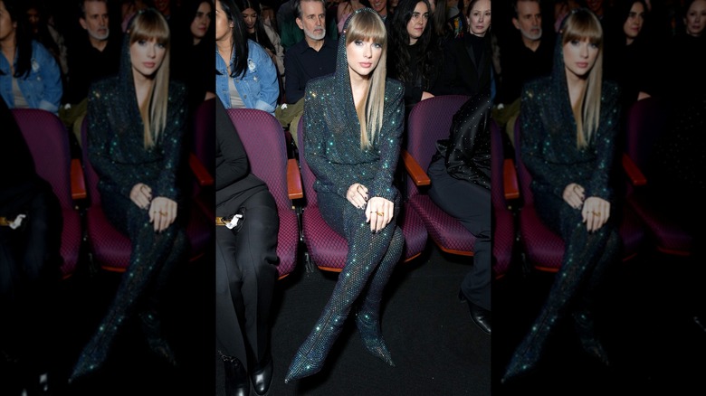 Taylor Swift seated in a hooded jumpsuit.