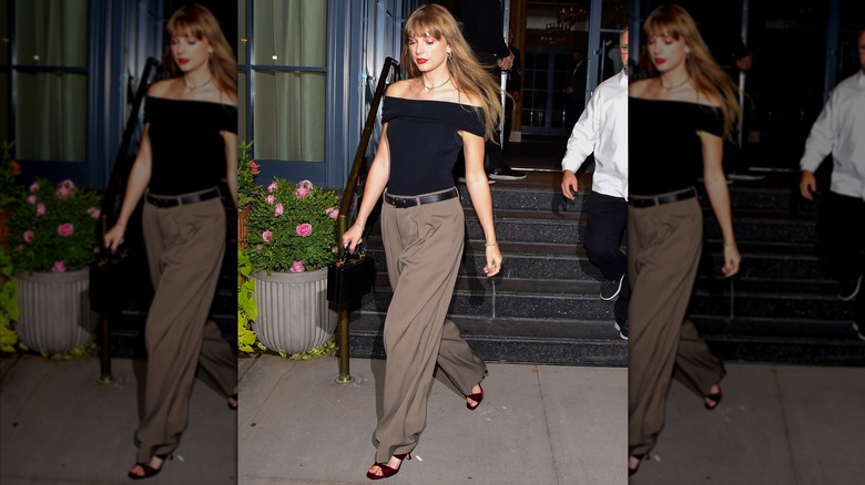 Taylor Swift wearing beige pants and a black off-the-shoulder top.