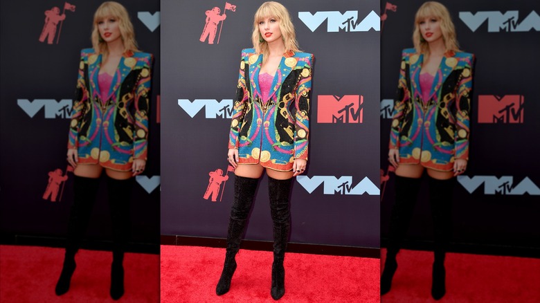 Taylor Swift posing in a patterned blazer and thigh-high black boots.