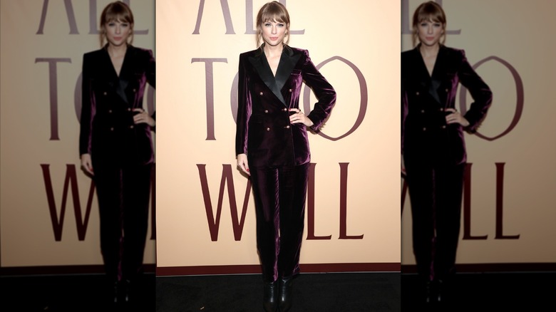 Taylor Swift posing with her hand on her hip in a purple velvet suit.