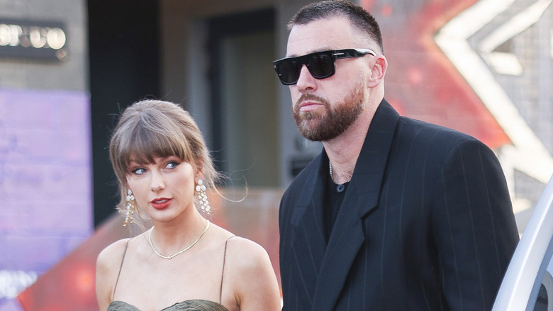 Taylor Swift in drop earrings with Travis Kelce in sunglasses and pinstripe suit