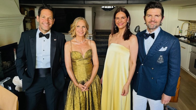 Adam Scott, in a navy blue suit jacket and white pants, with Paul Rudd, Julie Rudd, and Naomi Scott, all smiling