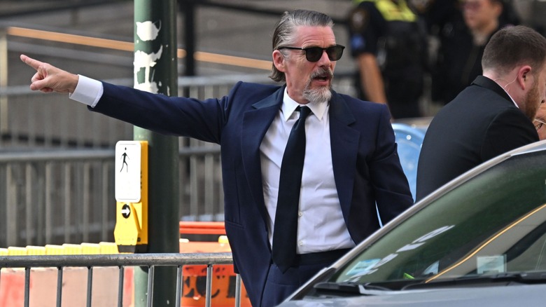 Ethan Hawke pointing, in a navy blue suit, on the street outside Madison Square Garden