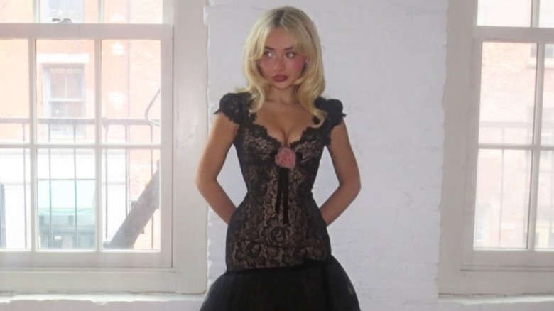 Sabrina Carpenter in a black lace dress with her hands behind her back