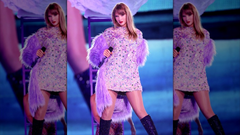 Taylor Swift in a purple dress and coat on stage in the Eras tour