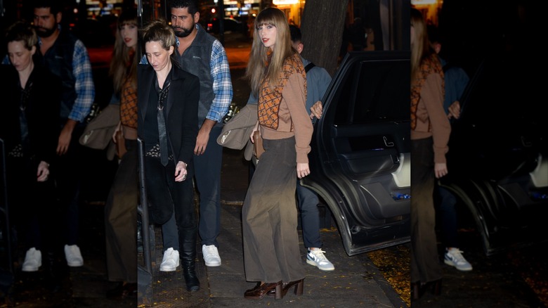 Taylor Swift in baggy dark pants with an orange sweater outside