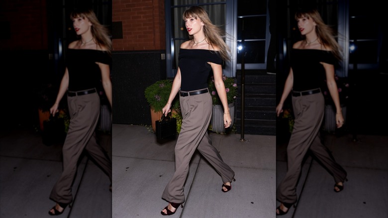 Taylor Swift in brown pants and a black top walking outside