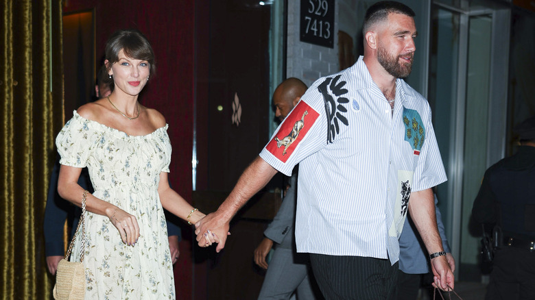 Taylor Swift smiling as she and Travis Kelce walk and hold hands.