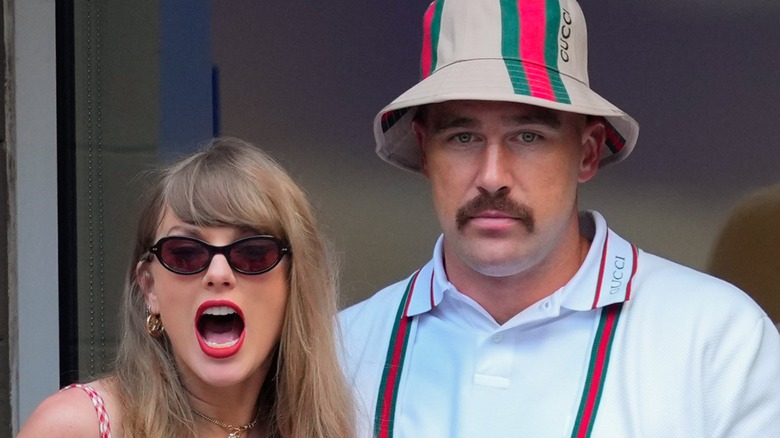 Taylor Swift open mouthed and wearing shades next to Travis Kelce in a Gucci shirt and bucket hat.