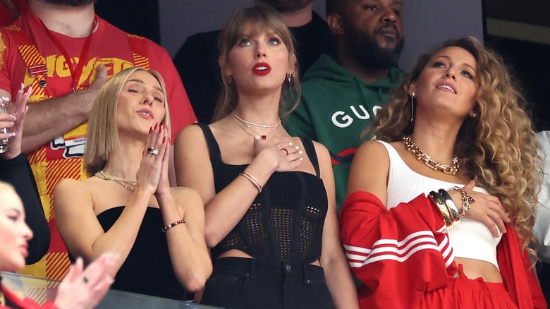 Taylor Swift looking up with her hand on her heart, surrounded by people.