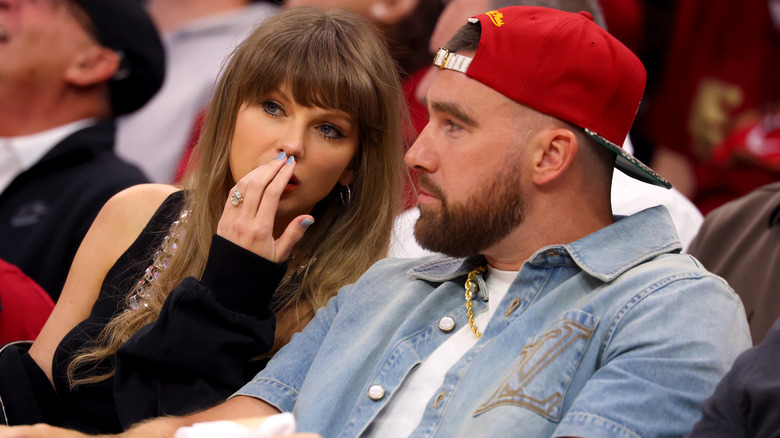 Taylor Swift speaking behind her hand to Travis Kelce at a New York Knicks game.