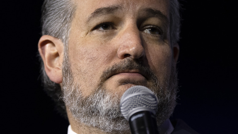 Ted Cruz standing at microphone with serious expression