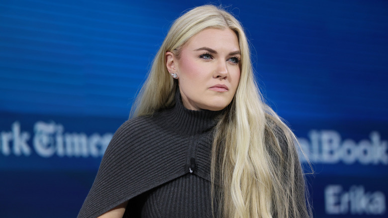 Erika Kirk squints while wearing a gray sweater dress, with her long, blonde hair covering one shoulder.