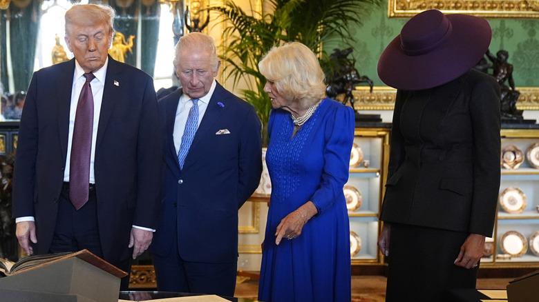 Donald Trump, King Charles III, Queen Camilla, and Melania Trump looking at artifacts, with Melania dressed in black and covering her face with a wide-brimmed hat