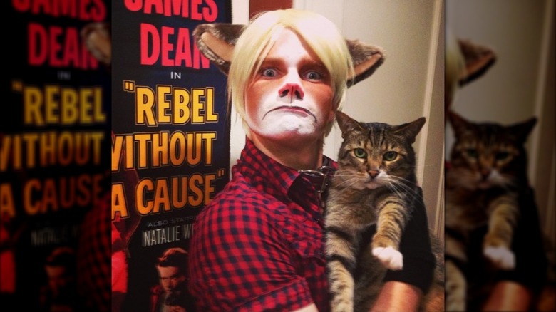 Chris Colfer wearing a Grumpy Cat costume with a blond wig and holding a cat