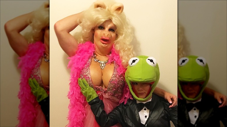 Colton Haynes wearing a Miss Piggy costume with prosthetic breasts and Ally Maki touching one while dressed as Kermit the Frog