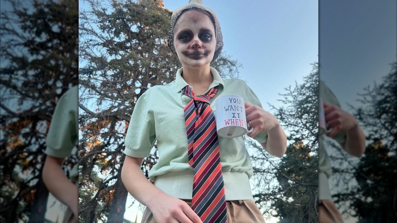 Joey King dressed like Flash Slothmore from "Zootopia" with sloth makeup and a striped tie and holding a mug outside