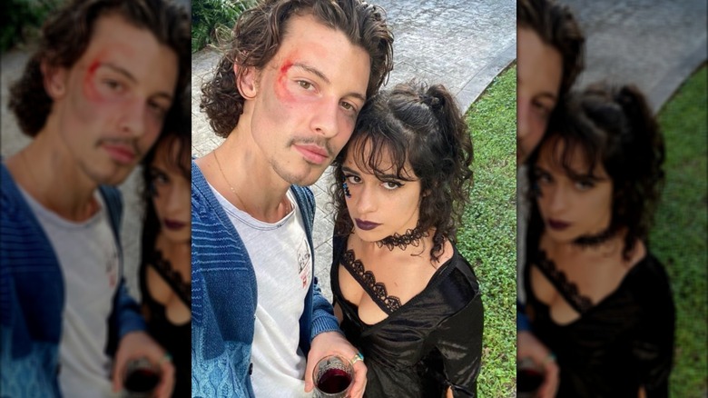Shawn Mendes with red makeup around one eye taking selfie outdoors with Camila Cabello